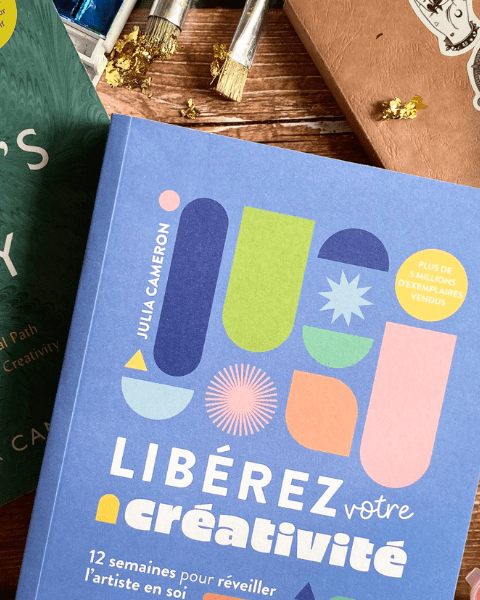 "The artist's way" ou "libérez votre créativité" en gros plan, entourés de crayons de couleurs, de peintures au numéro, d'un carnet, de pinceaux. Retrouvez toutes nos lectures sur Deliciously Home.
