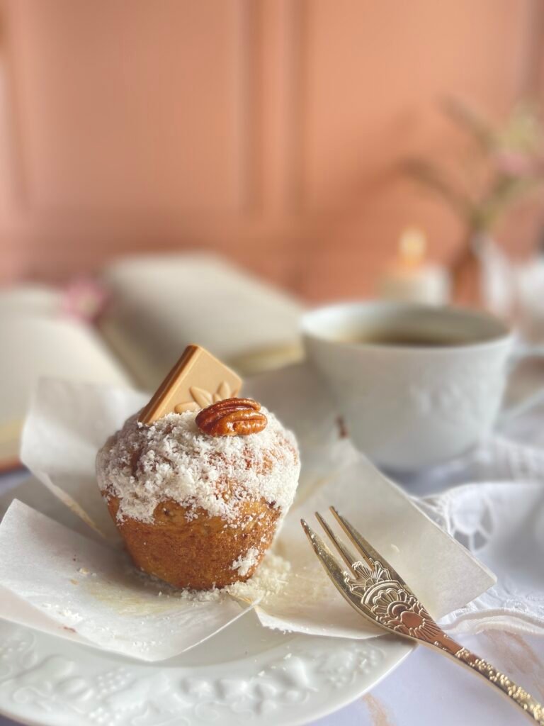 Muffins moelleux Dulcey coco pécan, une touche gourmande et réconfortante avec un livre ouvert et une bougie en arrière-plan. Recette sur Deliciously Home.