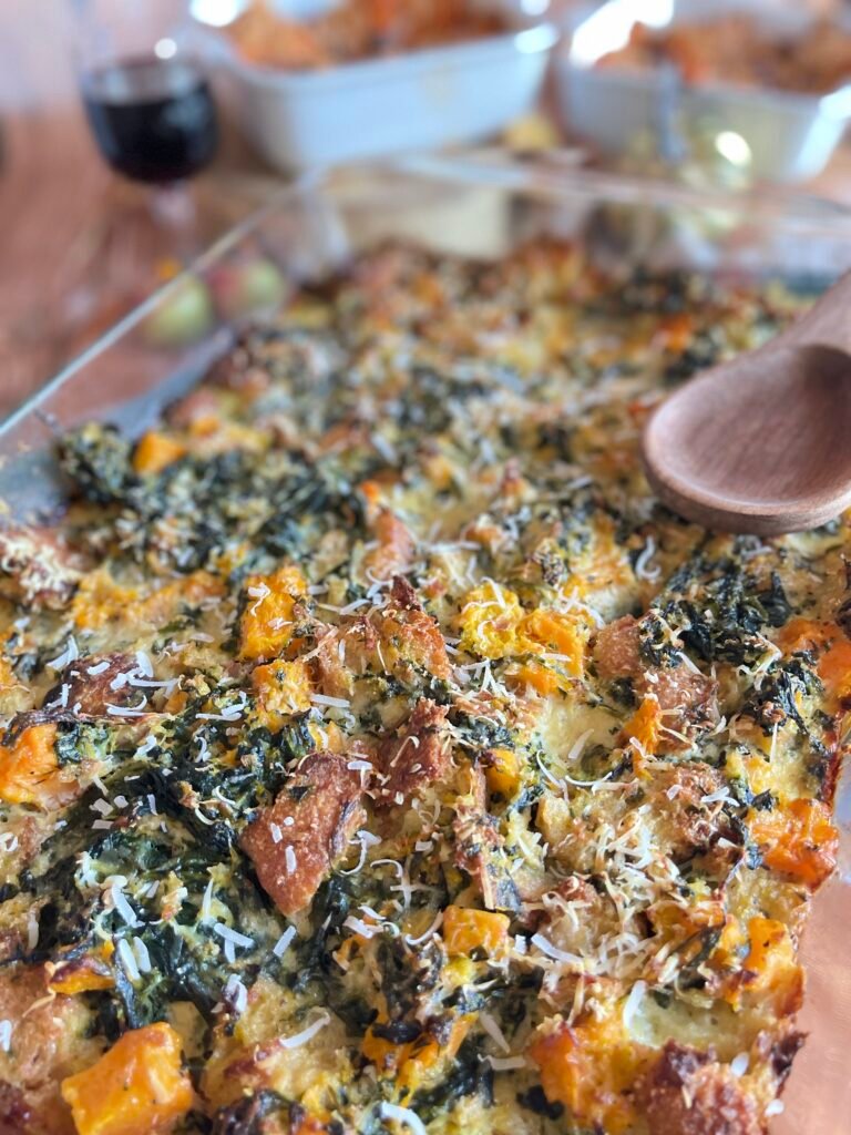 Un pudding salé à la courge et aux épinards, garni de parmesan râpé, avec une cuillère en bois prête à servir, entouré d'éléments de décoration automnale.