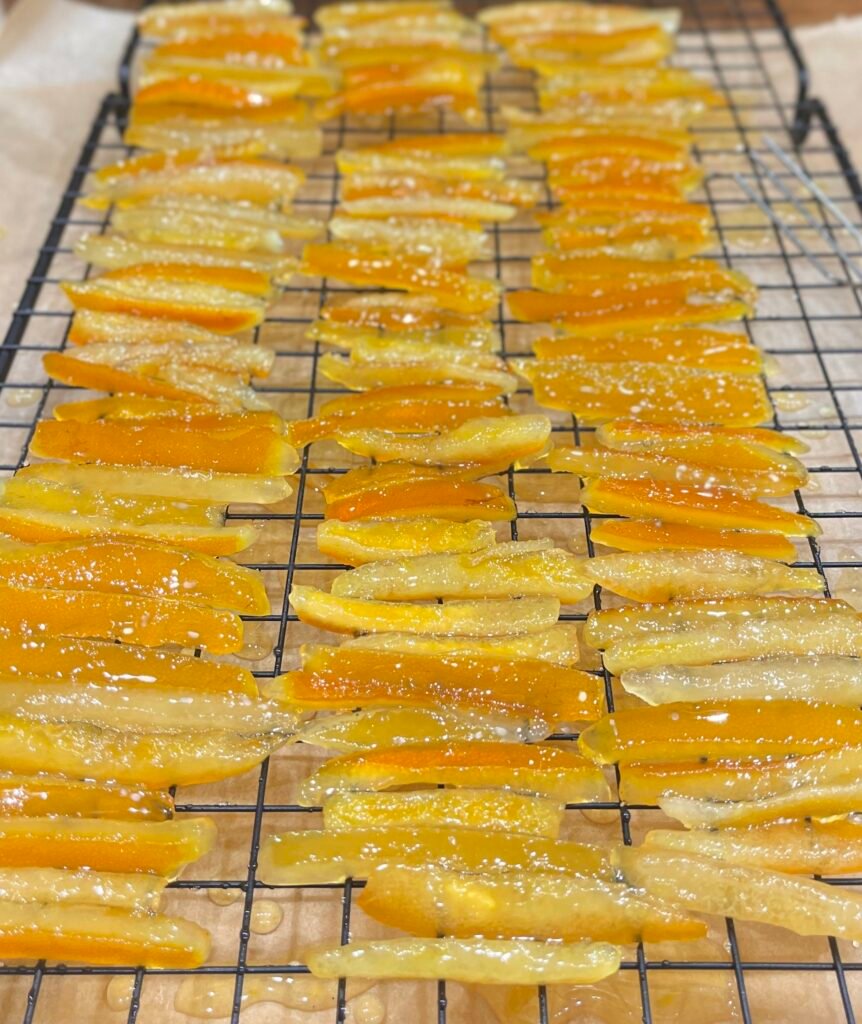 Écorces confites maison – morceaux d’écorces d’orange et de citron en cours de séchage sur une grille, brillants et pleins de saveurs. Recette sur Deliciously Home.