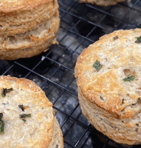 Gros plan sur des scones dorés et feuilletés, garnis de ciboulette hachée, refroidissant sur une grille. Recette sur Deliciously Home.