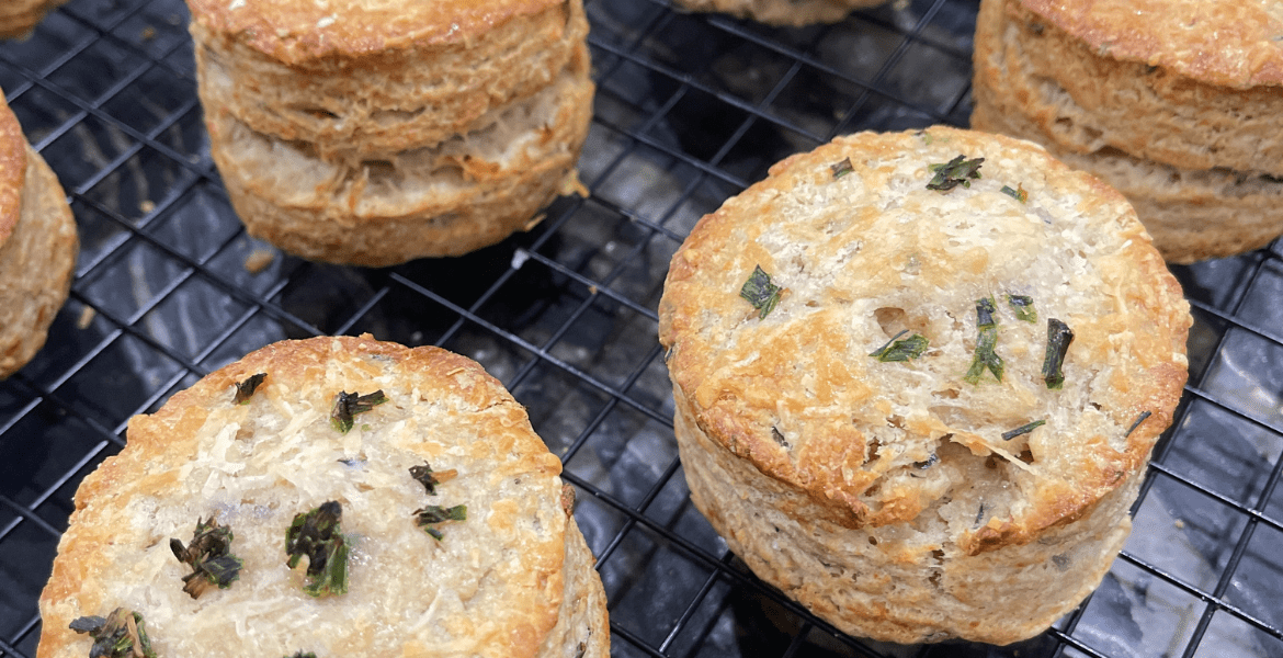 Gros plan sur des scones dorés et feuilletés, garnis de ciboulette hachée, refroidissant sur une grille. Recette sur Deliciously Home.