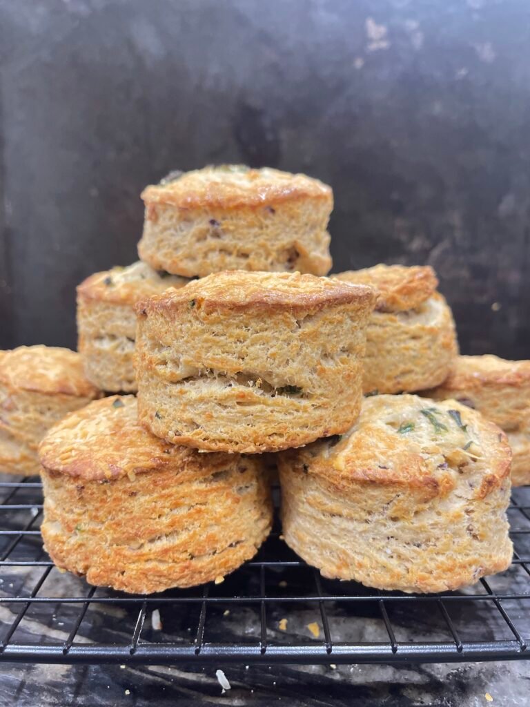 Une pyramide de scones dorés et feuilletés, montrant une texture moelleuse et croustillante, posée sur une grille noire avec un fond sombre.