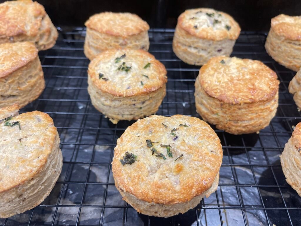 Une rangée de scones dorés et moelleux sur une grille de refroidissement, avec des détails de ciboulette et une texture feuilletée bien visible.