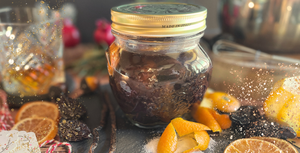 Gros plan sur un bocal de pruneaux à l'Armagnac fait maison entouré d'une décoration festive. Recette disponible sur Deliciously Home.