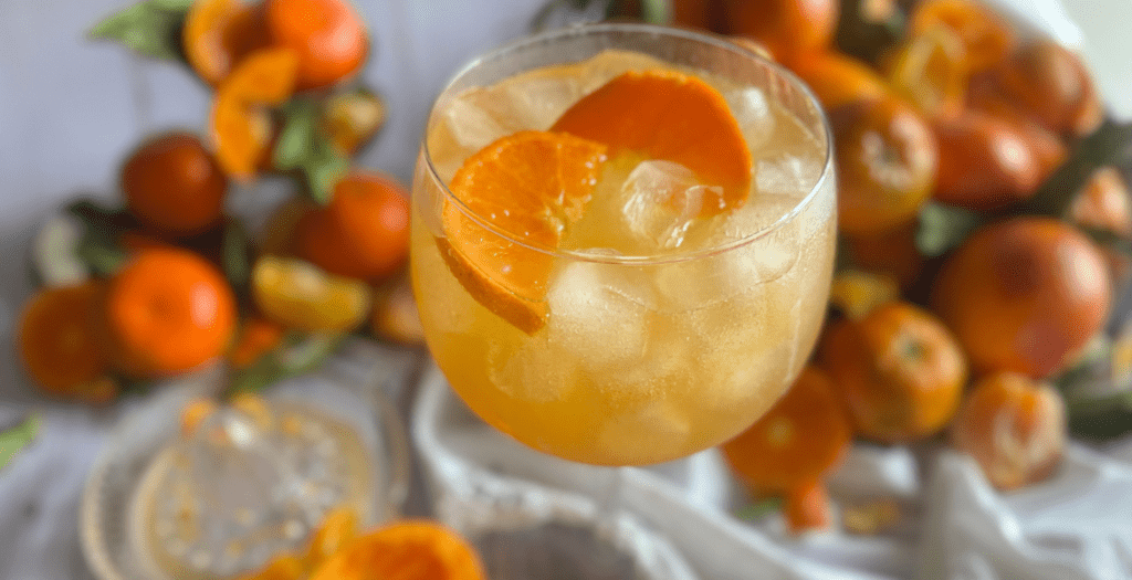 Cocktail spritz à la mandarine, rafraîchissant et légèrement acidulé, parfait pour l’hiver. Présentation dans un grand verre avec glaçons et rondelle d’agrumes. Recette disponible sur Deliciously Home.