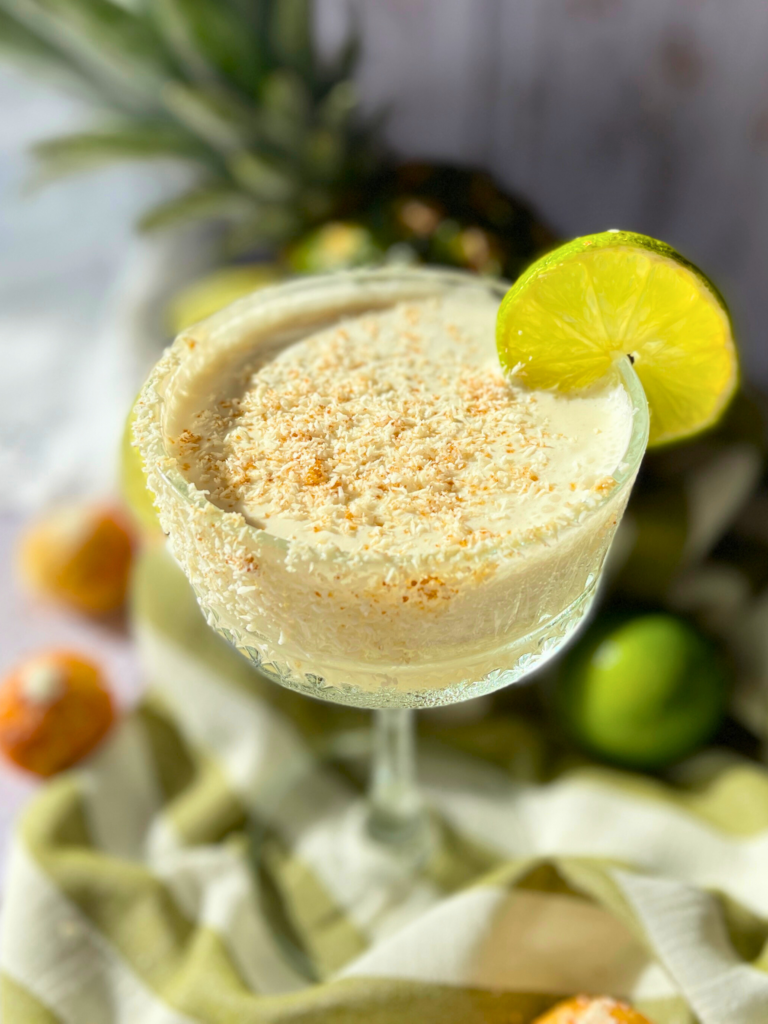 mocktail pina colada deliciouslyhome article2 Mocktail crémeux à l’ananas et noix de coco, bord du verre enrobé de coco râpée, tranche de citron vert en garniture, posé sur un linge rayé vert et blanc.