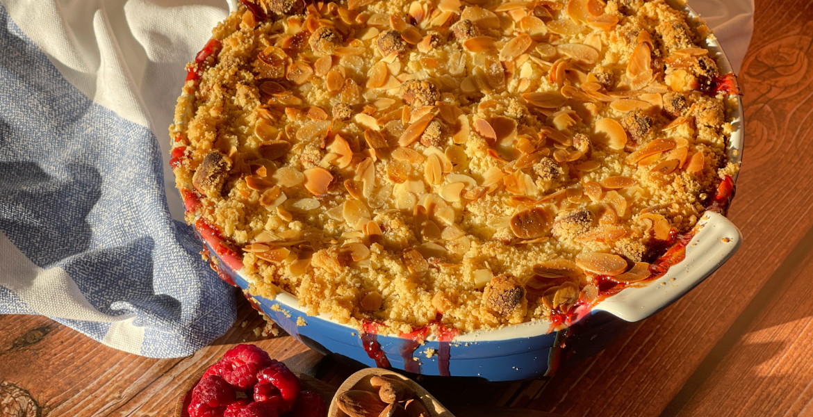 llustration du crumble d’automne rhubarbe-framboise-marzipan fraîchement sorti du four, avec ses amandes effilées dorées et son jus légèrement caramélisé : un visuel évocateur de la chaleur réconfortante de cette recette signée Deliciously Home.