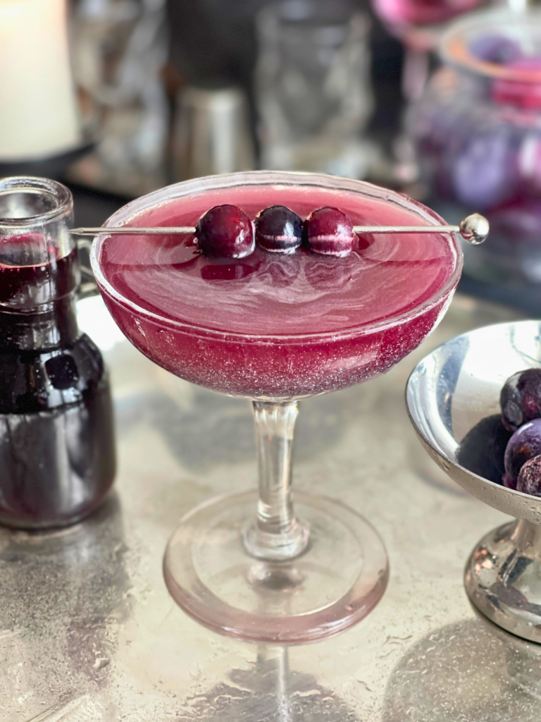 blueberry sour cocktail deliciouslyhome article1 Whiskey sour aux myrtilles dans une coupe, reflets pailletés violets, recette Halloween signée Deliciously Home.