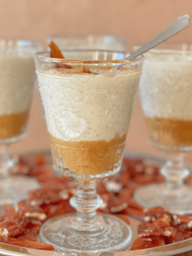 Coupes de riz au lait vanillé déposées sur une compotée de pommes caramélisées, décorées de morceaux de caramel aux noix. Un visuel évocateur du dessert doudou partagé sur Deliciously Home.