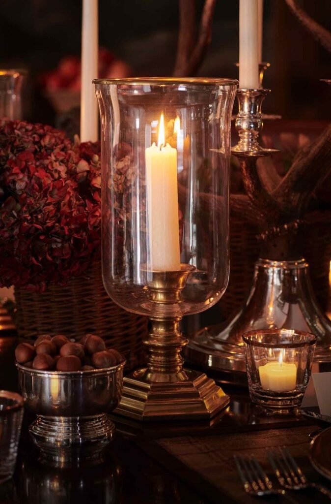 Bougeoir en laiton doré avec grande bougie blanche, entouré de fruits secs et de fleurs séchées dans un décor feutré de Noël façon Ralph Lauren.