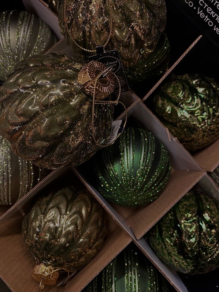 Boules de Noël vert sapin et bronze, décorées de paillettes dorées, disposées en boîte — des ornements luxueux rappelant l’univers Ralph Lauren.