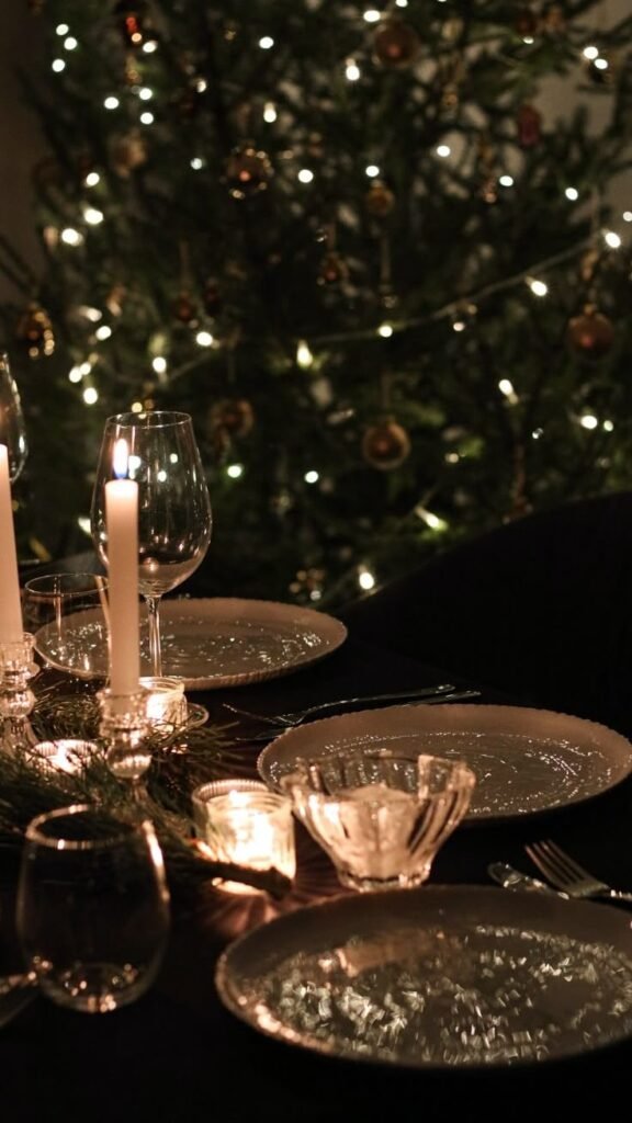 Table de fête minimaliste et élégante, dressée avec vaisselle blanche et bougies, en arrière-plan un sapin décoré — ambiance intimiste et chaleureuse.