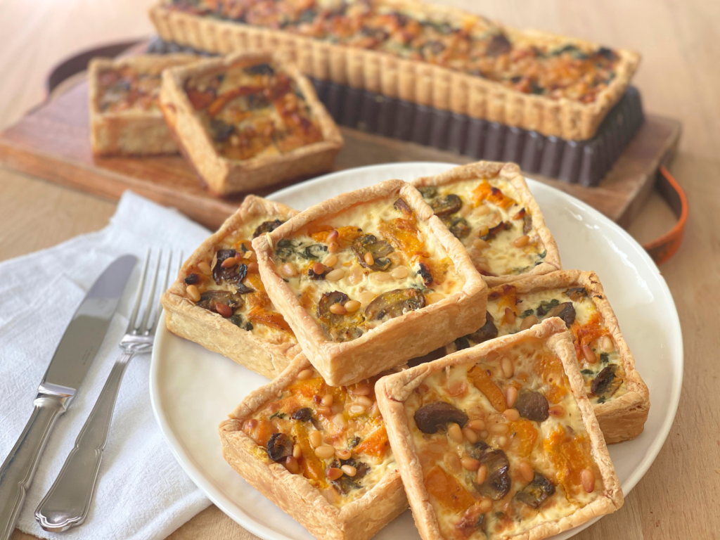 Vue en perspective des quiches carrées encore tièdes, empilées comme on aime le faire quand on reçoit. Une invitation directe au partage autour d’un plat d’automne simple, chaleureux, et fait maison. Une recette Deliciously Home.