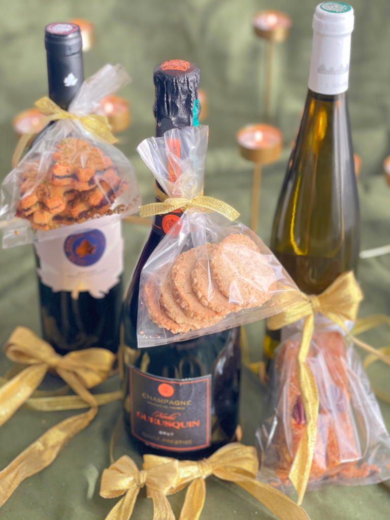Mise en scène Deliciously Home montrant les trois biscuits de la Cookie Box Express: shortbread romarin-citron-pecan, sapins cranberry-pistache-olive et biscuits gorgonzola-noix, présentés comme cadeaux gourmands pour accompagner une bouteille de vin, dans l’esprit de "Biscuits de Noël salés : 3 recettes pour des apéritifs festifs".