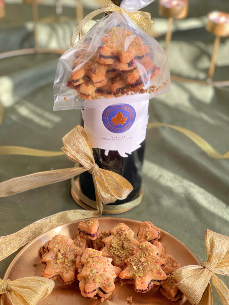 Illustration Deliciously Home mettant en avant les sapins apéritifs cranberry-pistache-olive, l’un des trois biscuits de la Cookie Box Express décrite dans "Biscuits de Noël salés : 3 recettes pour des apéritifs festifs", montrés ici comme idée de cadeau salé à offrir avec une bouteille de vin.