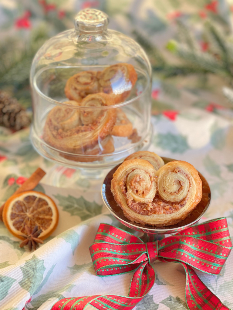 Palmiers pécan-cannelle à la pâte feuilletée dorée, présentés en mise en scène de fête pour illustrer l’une des 3 recettes de biscuits de Noël sucrés à offrir sur Deliciously Home.
