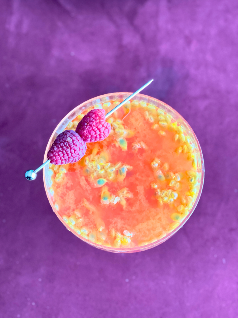 Margarita au fruit de la passion et à la framboise présentée parmi le sirop maison et les fruits, un cocktail détaillé sur Deliciously Home.