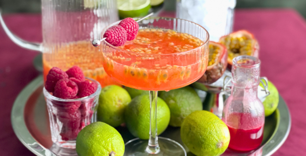 Margarita au fruit de la passion et à la framboise entourée de ses ingrédients frais, un cocktail que l’on retrouve dans l’article de Deliciously Home.