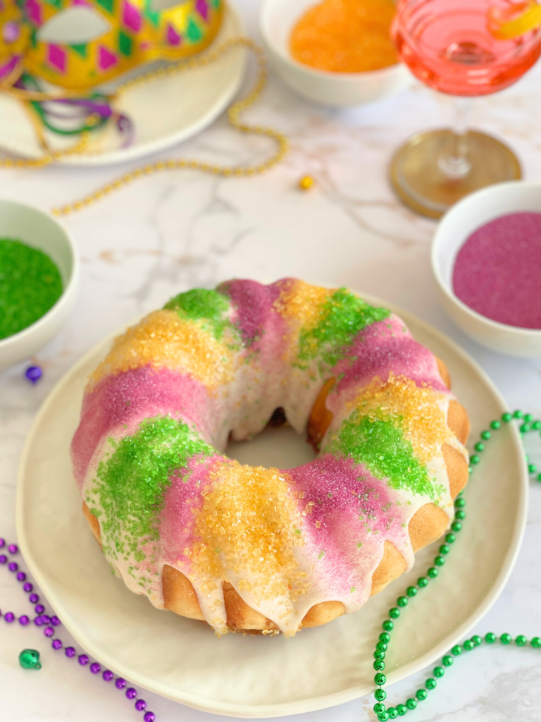 Brioche de Mardi Gras - King Cake aux couleurs traditionnelles du carnaval de La Nouvelle-Orléans, glaçage coulant et sucres décoratifs, ambiance festive. Une recette Deliciously Home.
