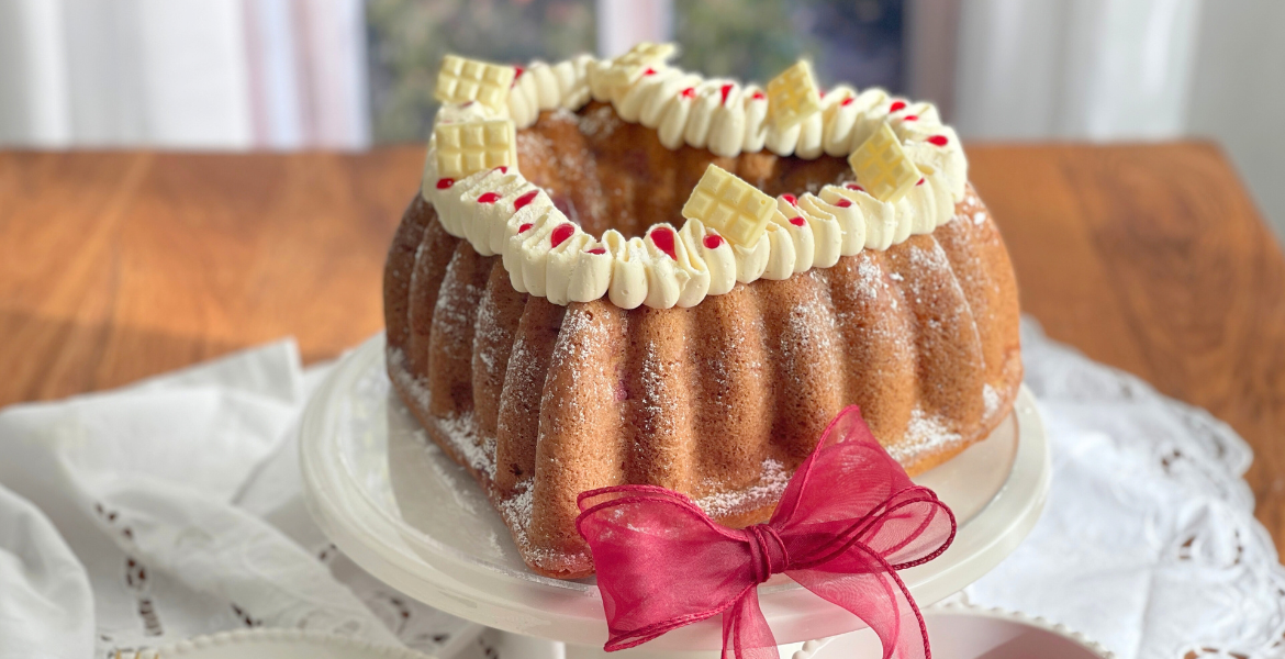 Cake framboise chocolat blanc présenté sur son présentoir, moelleux et décoré pour février, recette gourmande disponible sur Deliciously Home.