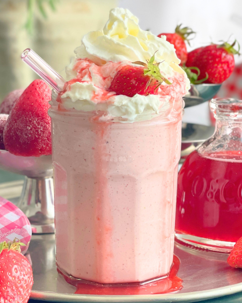 Milkshake fraise vanille servi dans un pot en verre avec chantilly, fraise fraîche et sirop de fraise, ambiance rétro
