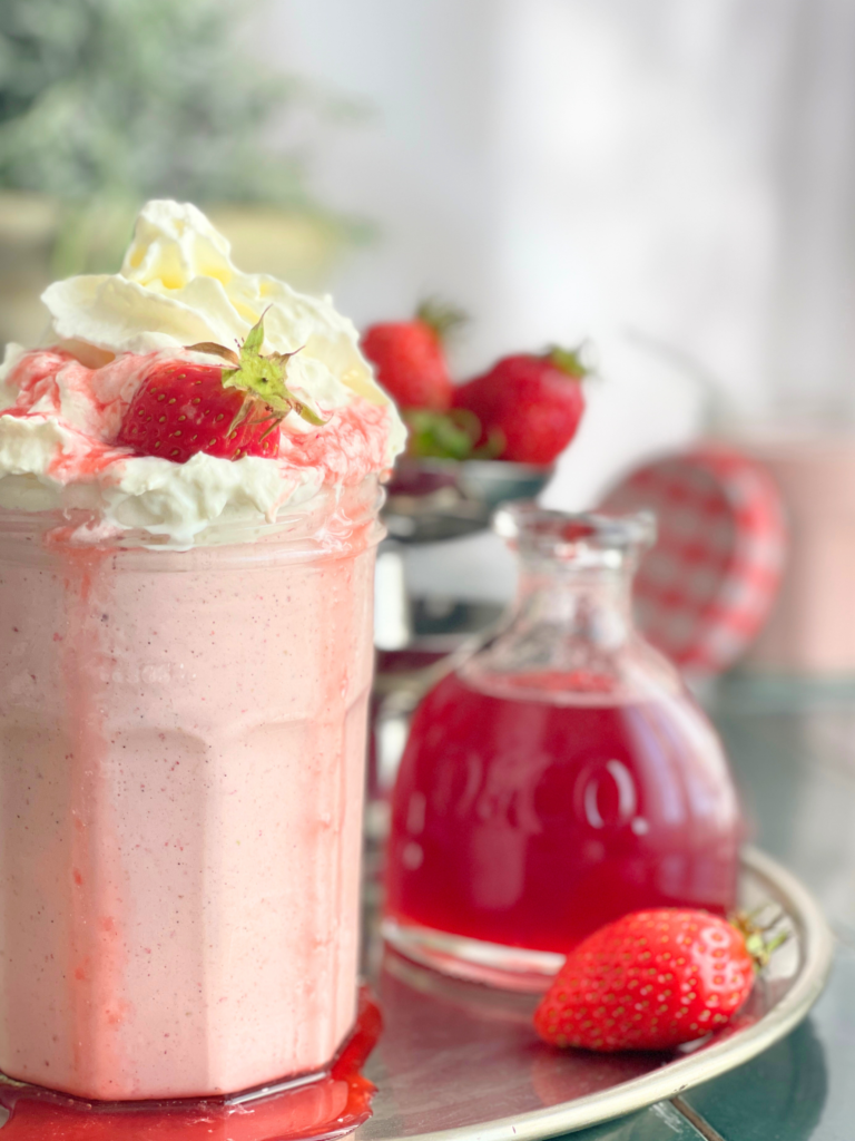 Milkshake fraise vanille avec sirop de fraise maison en arrière-plan et fraises fraîches autour