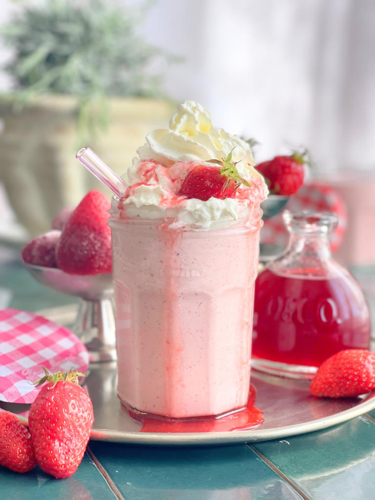 Milkshake fraise vanille maison avec chantilly et sirop, présenté sur un plateau avec fraises fraîches et pot de confiture