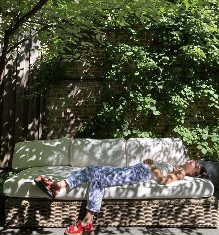 Canapé extérieur en rotin avec personne allongée à l’ombre dans un jardin verdoyant en été, à retrouver dans notre article sur Aménager un coin d’été chez soi sur Deliciously Home