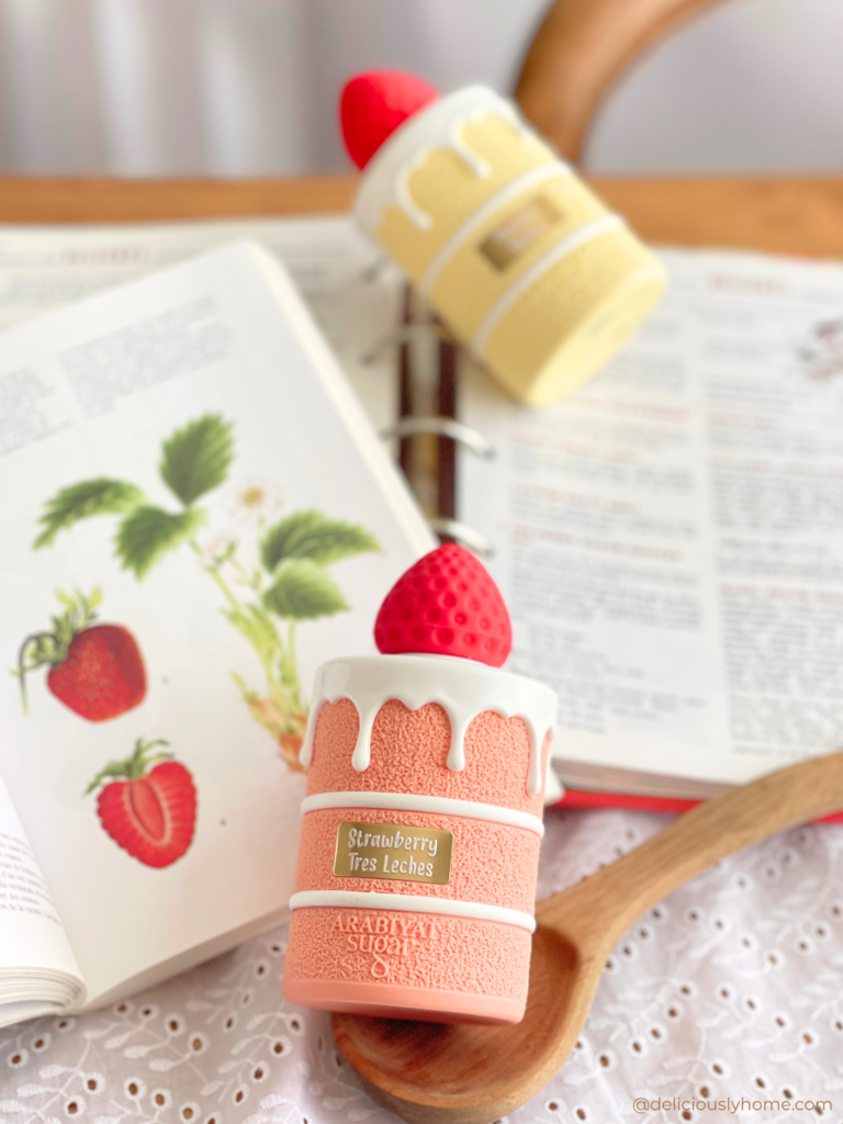 Deux parfum de la maison Arabiyat dont Sugar Strawberry Tres Leches entourés de livres de cuisine et d’ustensiles, dans l’ambiance de nos strawberry days, en écho à notre article DeliciouslyHome où nous décrivons l’odeur du parfum et ses notes gourmandes de fraise et de lait.