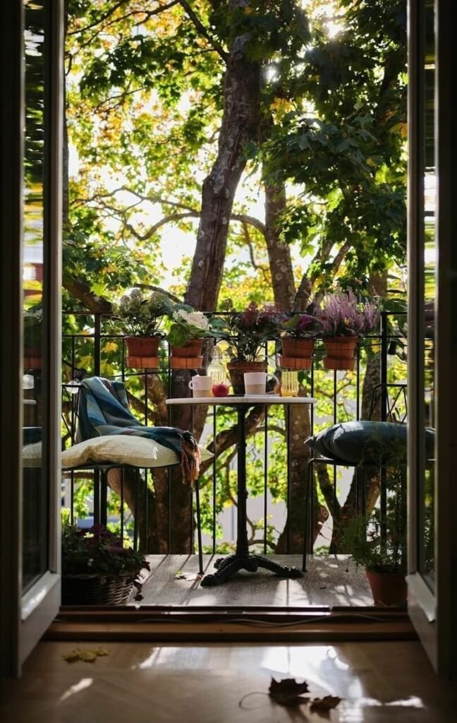 Balcon cosy avec table ronde, chaises et plantes en pots sous la lumière d’été, à voir dans notre article sur Aménager un coin d’été chez soi sur Deliciously Home