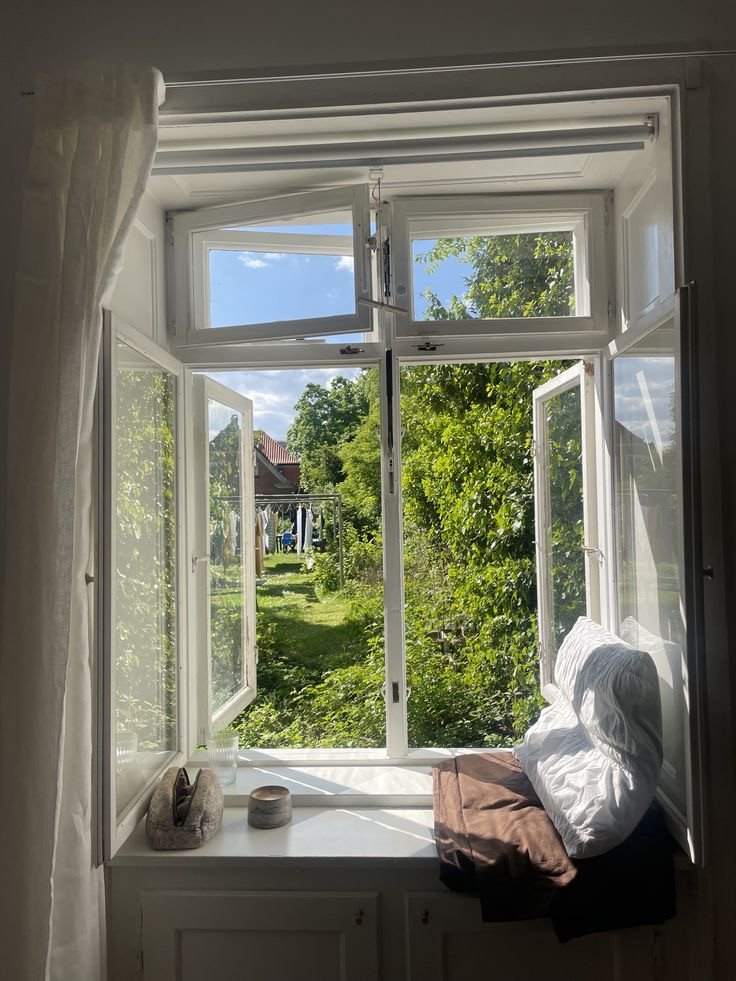 Fenêtre ouverte avec vue sur un jardin et espace détente aménagé à l’intérieur, à découvrir dans notre article sur Aménager un coin d’été chez soi sur Deliciously Home