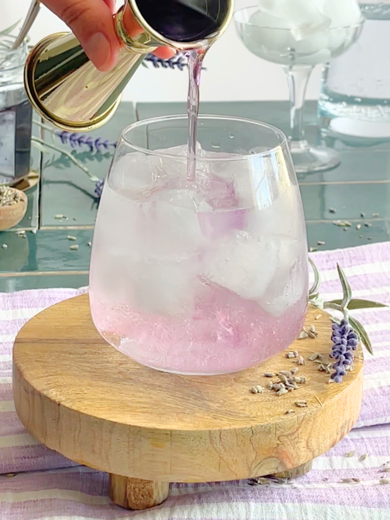 Préparation d’un gin tonic lavande maison avec sirop de lavande et tonic versé sur glaçons. Une recette cocktail fraîche et botanique créée par Deliciously Home.