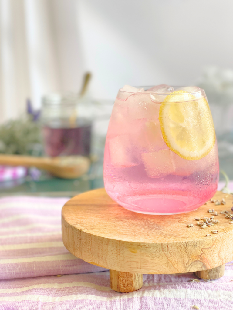 Verre de gin tonic rose à la lavande décoré de citron et servi bien frais. Un cocktail élégant et floral proposé par Deliciously Home pour les soirées d’été.