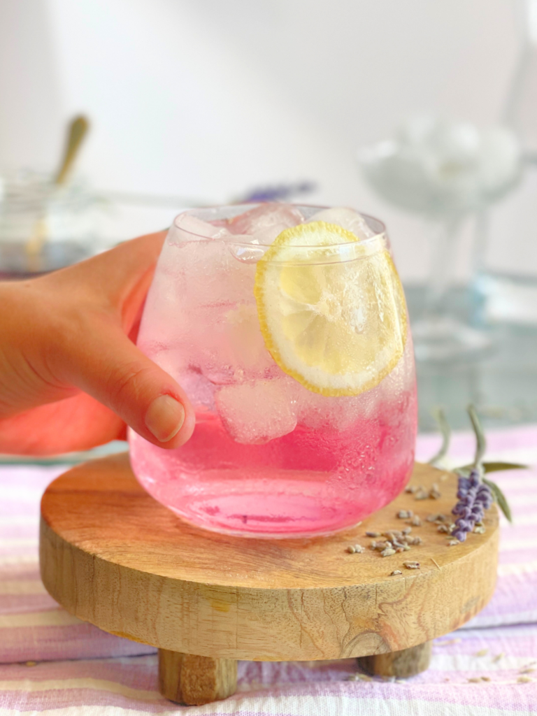 Main tenant un cocktail gin tonic lavande glacé préparé avec citron frais et sirop de lavande maison. Une recette estivale signée Deliciously Home.
