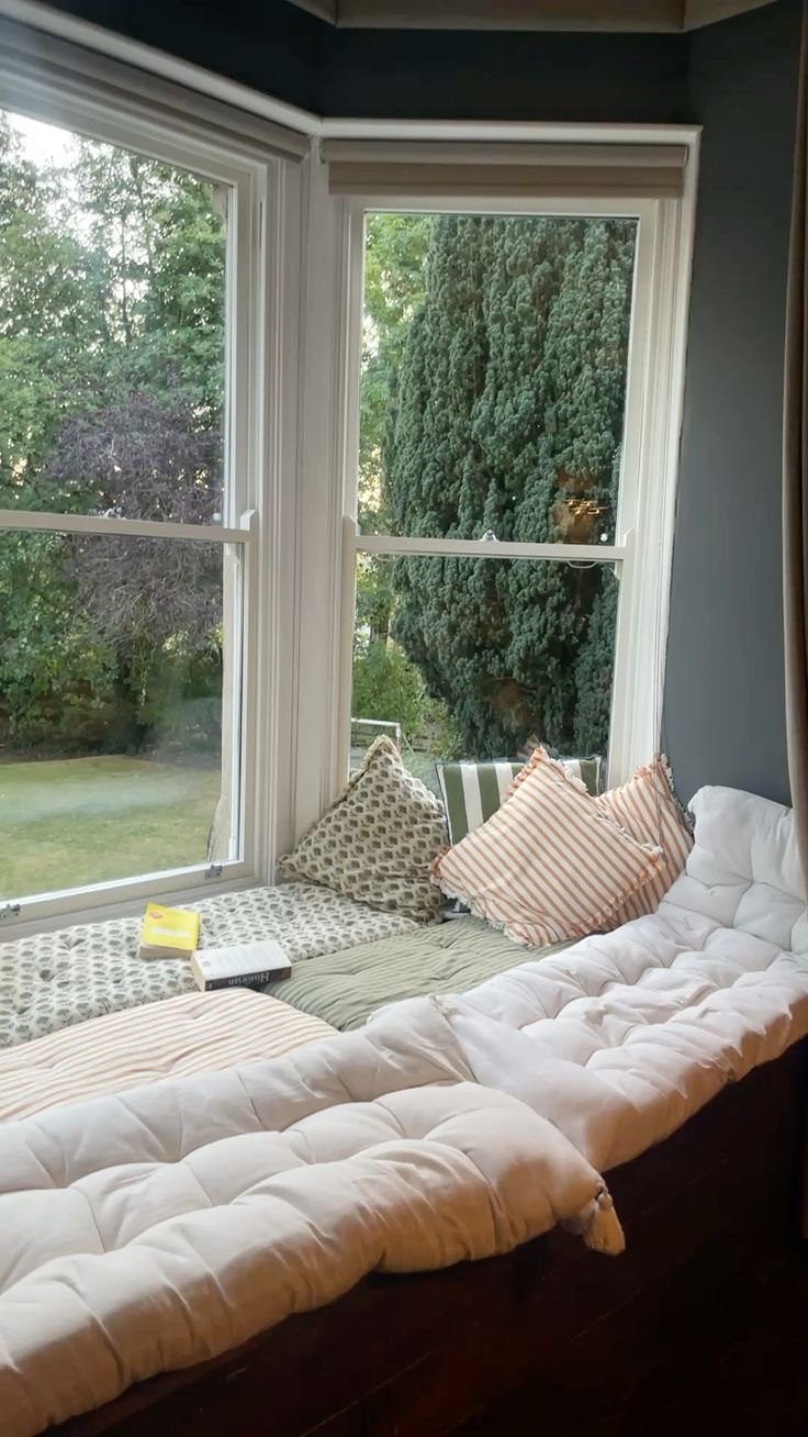 Banquette sous fenêtre avec matelas épais et coussins pour un coin lecture lumineux et cosy, à découvrir dans notre article sur Aménager un coin d’été chez soi sur Deliciously Home