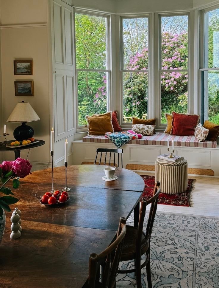 Salle à manger avec grande fenêtre et banquette intégrée offrant une vue sur jardin fleuri, à retrouver dans notre article sur Aménager un coin d’été chez soi sur Deliciously Home