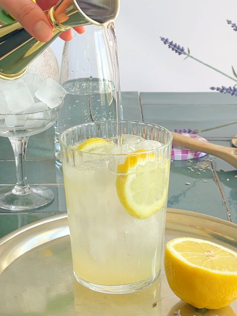 Préparation d’une limonade à la lavande avec sirop maison versé sur citron frais et glaçons. Une recette désaltérante et parfumée créée par Deliciously Home.