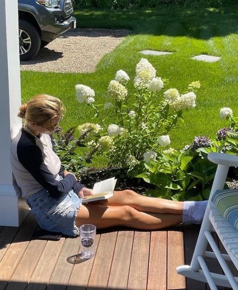 Femme lisant sur une terrasse ensoleillée entourée de fleurs et de verdure en été, à retrouver dans notre article sur Aménager un coin d’été chez soi sur Deliciously Home