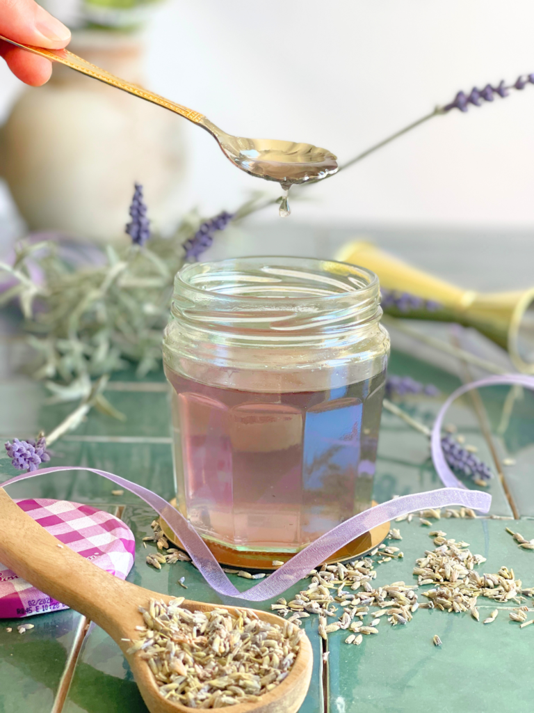 Cuillère de sirop de lavande maison au-dessus d’un bocal floral. Découvrez la recette sur Deliciously Home.