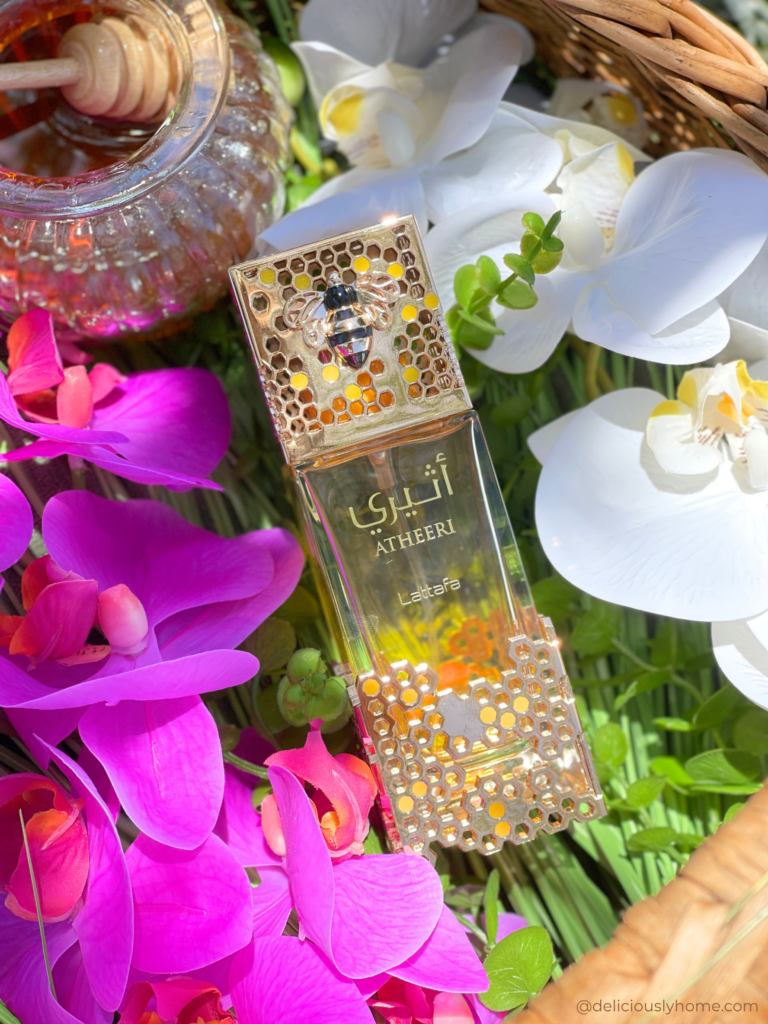 Flacon d'Atheeri de Lattafa parmi les orchidées et les fleurs printanières. Une composition signée Deliciously Home évoquant la fraîcheur florale et la lumière douce qui caractérisent ce parfum de printemps.