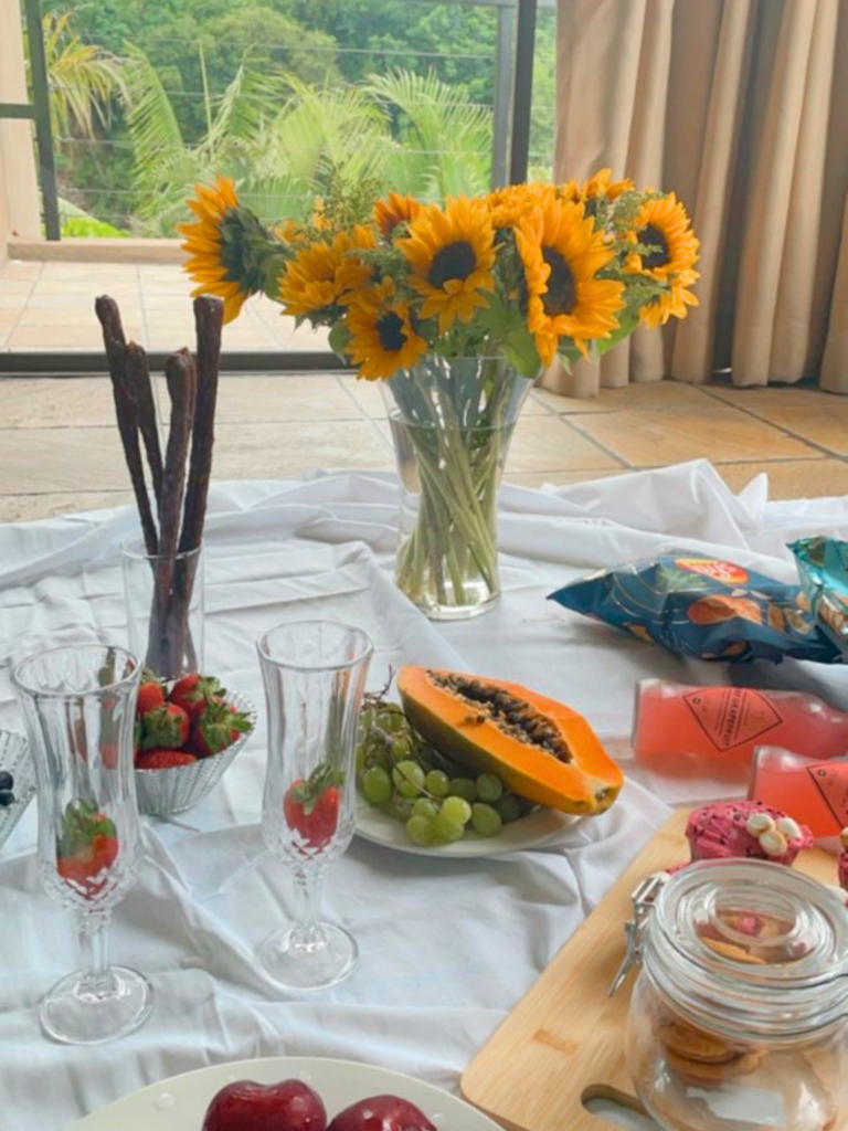 L’esprit du pique-nique ne se limite pas à l’extérieur : devant une baie vitrée ouverte, quelques fruits, des fleurs et une nappe suffisent à inviter l’été chez soi. À découvrir avec Deliciously Home
