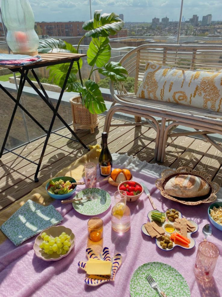 Créer une ambiance pique-nique en ville passe aussi par l’art de s’installer autrement : une nappe au sol, de la jolie vaisselle et la lumière du soleil sur une terrasse. À découvrir avec Deliciously Home