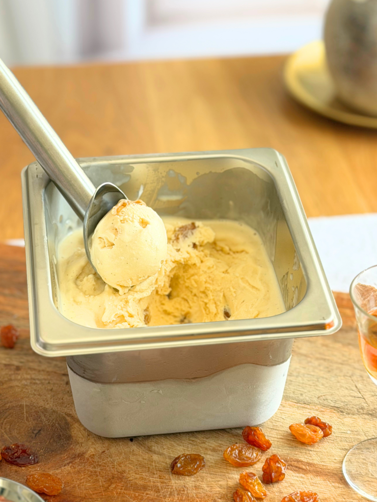 Bac de glace rhum-raisin maison avec une boule de glace crémeuse et des raisins secs. Recette à découvrir sur Deliciously Home.