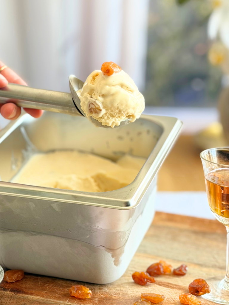 Gros plan sur une boule de glace rhum-raisin maison avec un raisin macéré et une texture bien crémeuse. Recette à découvrir sur Deliciously Home.