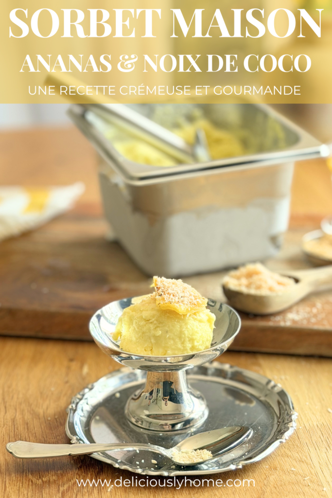Pin Pinterest présentant un sorbet Piña Colada maison à l'ananas et à la noix de coco. Une boule de sorbet est servie dans une coupe avec un morceau d'ananas rôti et de la noix de coco râpée. Le texte annonce une recette crémeuse et gourmande. Découvrez la recette complète sur Deliciously Home.