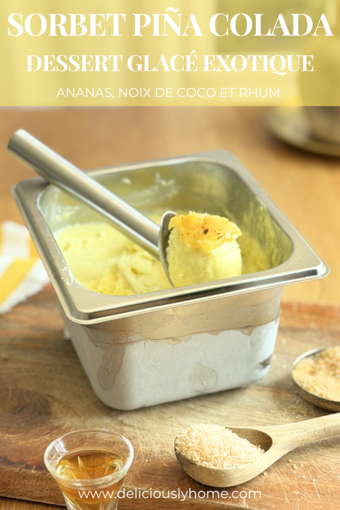 Pin Pinterest d'un sorbet Piña Colada maison. Une boule de sorbet garnie d'un morceau d'ananas rôti est présentée dans un bac en inox, accompagnée de noix de coco râpée et de rhum. Le texte met en avant un dessert glacé exotique à l'ananas, à la noix de coco et au rhum. Découvrez la recette complète sur Deliciously Home.