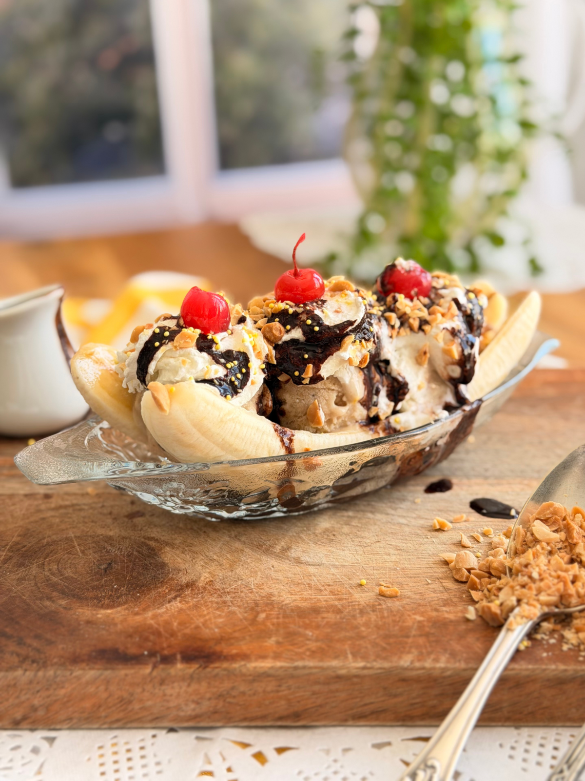 Banana split maison servi dans une coupe en verre, avec glace aux bananes rôties, chantilly, chocolat chaud, cacahuètes et cerises. Recette à découvrir sur Deliciously Home.