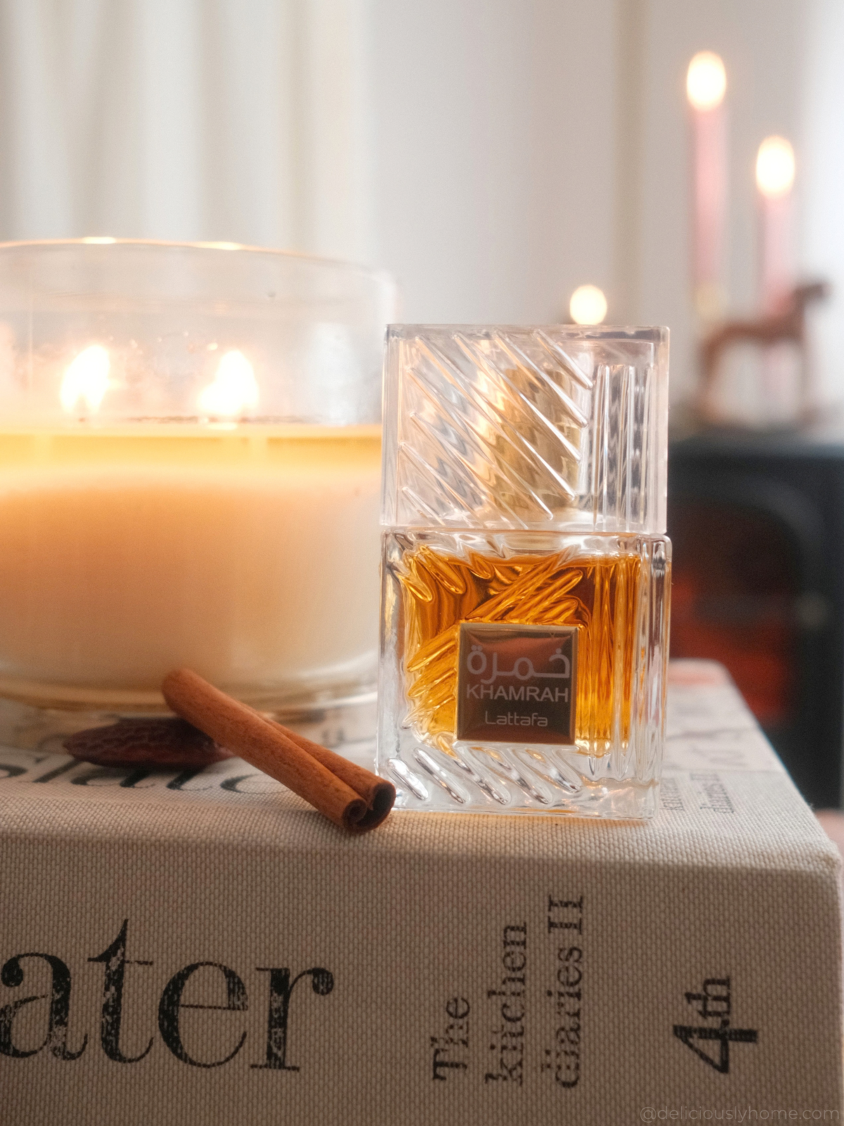 Khamrah de Lattafa, parfum d’automne épicé et gourmand, entouré de bougies et de cannelle pour évoquer les plaisirs de la saison sur Deliciously Home.