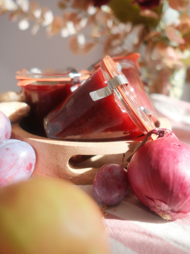 Pots de chutney de prunes disposés avec des prunes, du gingembre et un oignon rouge, recette Deliciously Home.